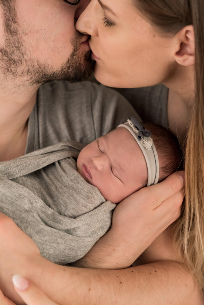 Baby im Arm der sich küssenden Eltern