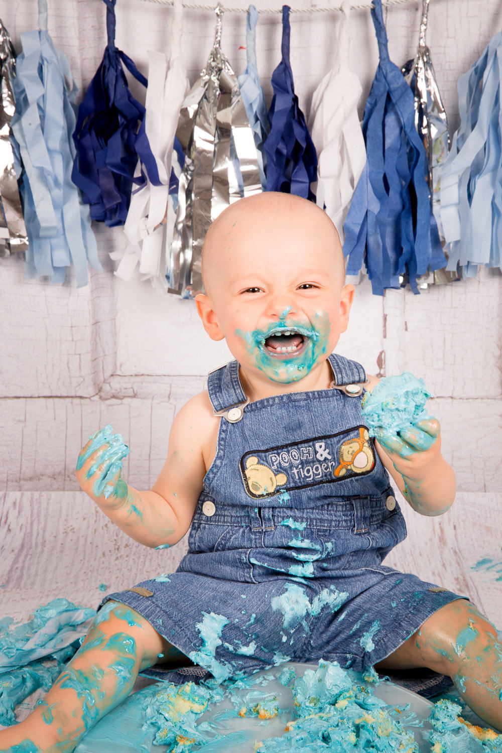 Junge beim Cake Smash Shooting lacht herzhaft mit Kuchen in der Hand