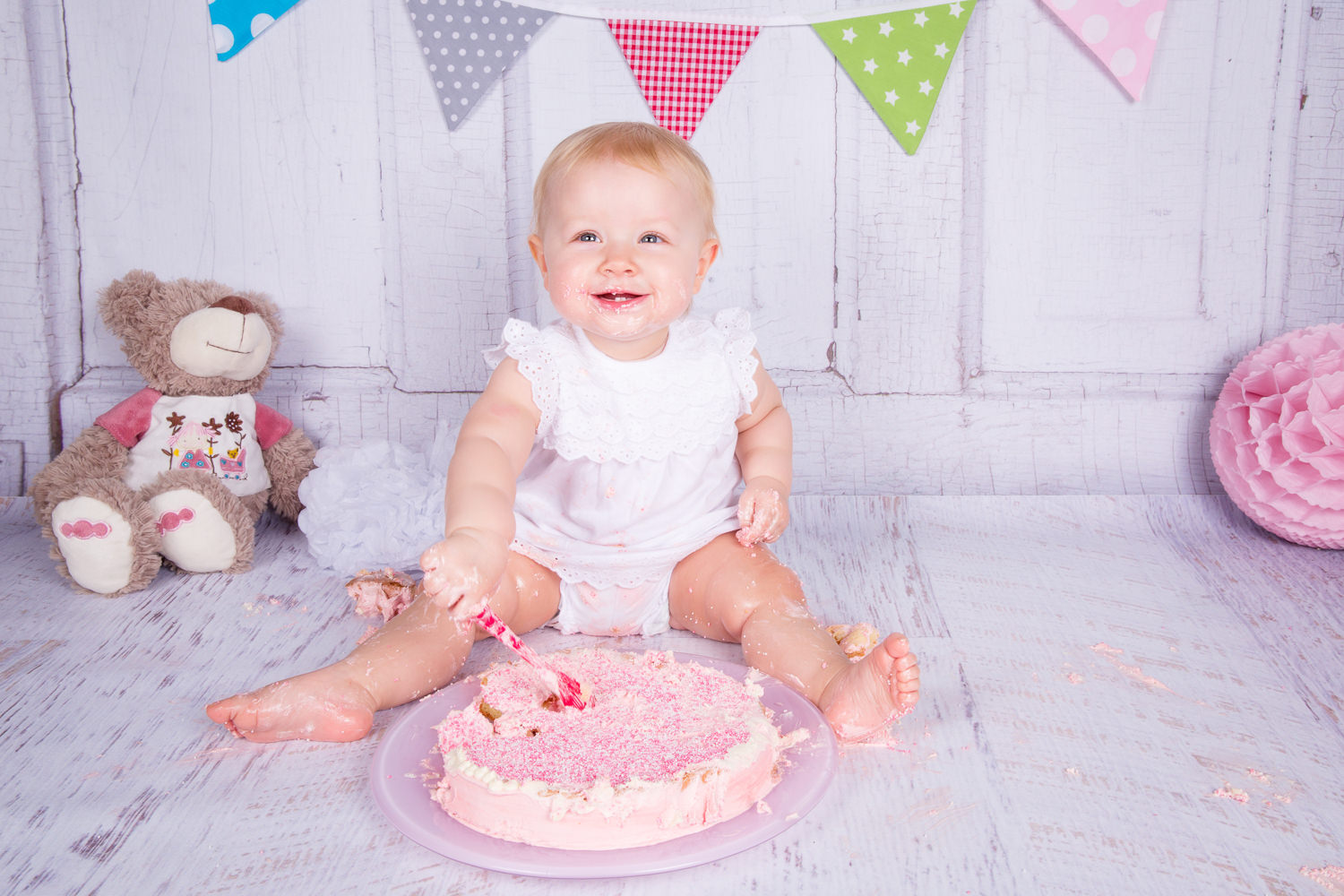 Einjähriges Mädchen beim Cake Smash Shooting mit rosa Kuchen