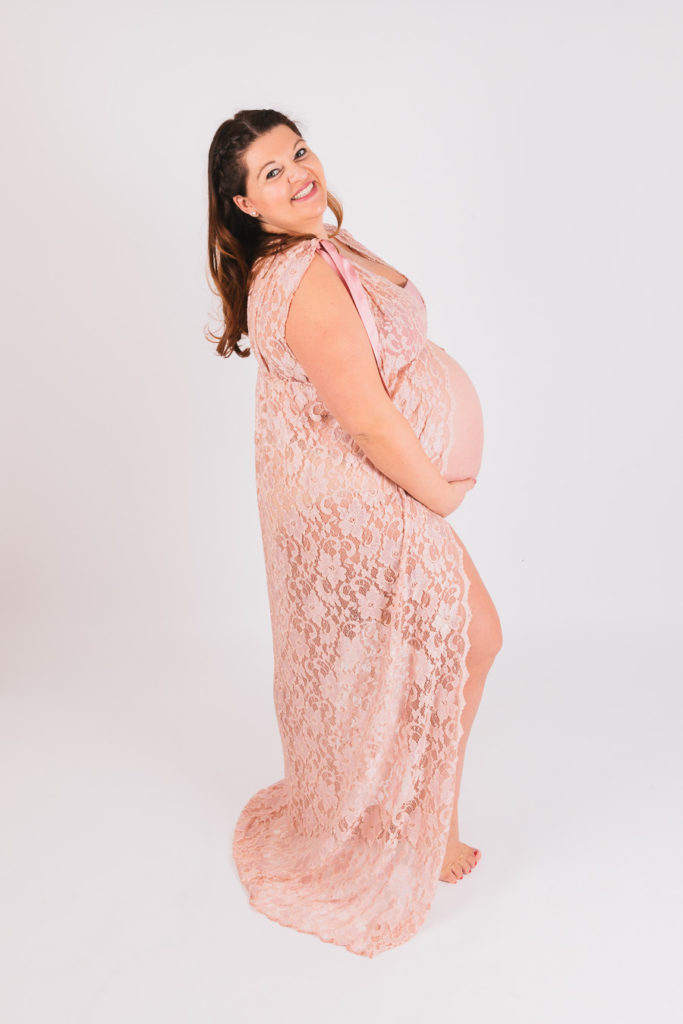 Studioportrait einer werdenden Mutter im rosa Spitzenkleid mit Babybauch