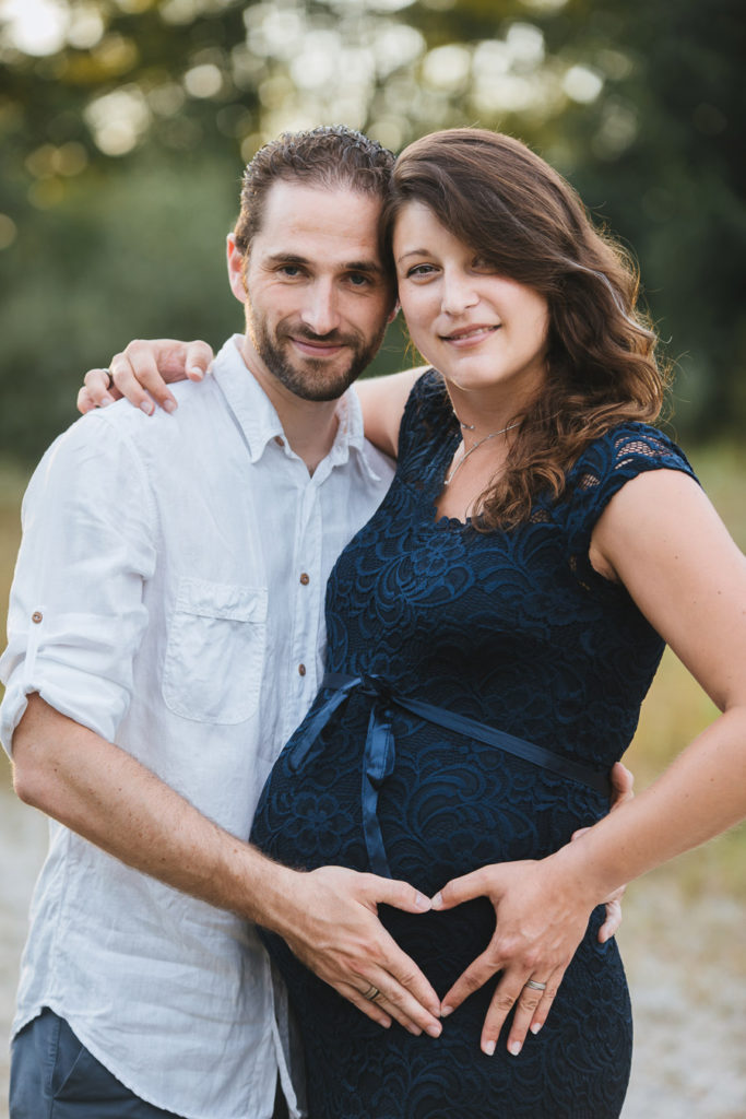 Paarfoto mit Babybauch und Herz-Händen